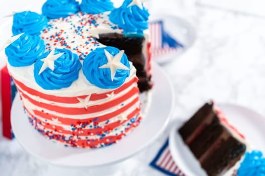 Slicing July 4th chocolate cake decorated with red, white, and blue buttercream frosting.