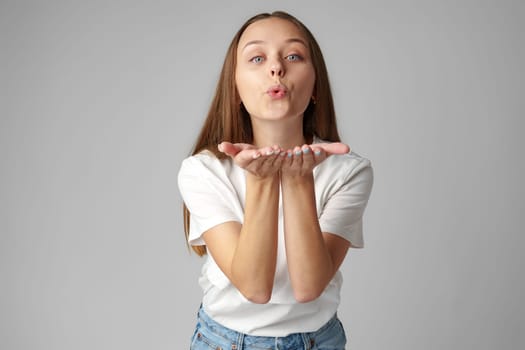 Young woman blowing a kiss to camera on gray background studio shot