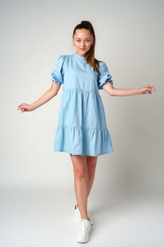 Young happy smiling woman in a light blue dress on a gray background close up