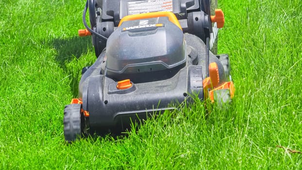 Castle Rock, Colorado, USA-June 25, 2023- At a residential suburban house, a lush green lawn is meticulously mowed using an electric lawn mower, creating a well-manicured and inviting outdoor space.