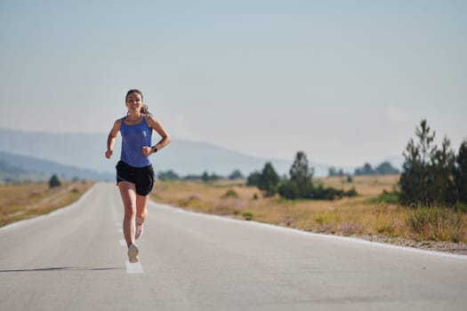 An athletic woman finds freedom and joy in a healthy lifestyle, running through a beautiful road trail at sunrise.