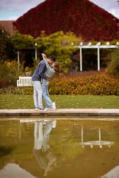 A couple in love hugs on the shore of a city pond in the European town. love story against the backdrop of autumn nature. romantic ambiance, couple goals, outdoor romance, seasonal charm, love in the city, autumnal vibes, European town, city pond, affectionate bonding, love story