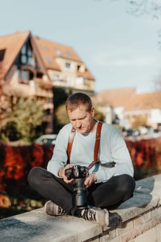 Man Sitting on Stairs in Old European City And Holding Photo Camera. Contemporary Stylish Blogger And Photographer