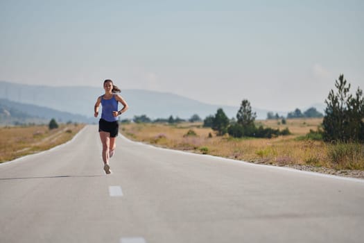 An athletic woman finds freedom and joy in a healthy lifestyle, running through a beautiful road trail at sunrise.