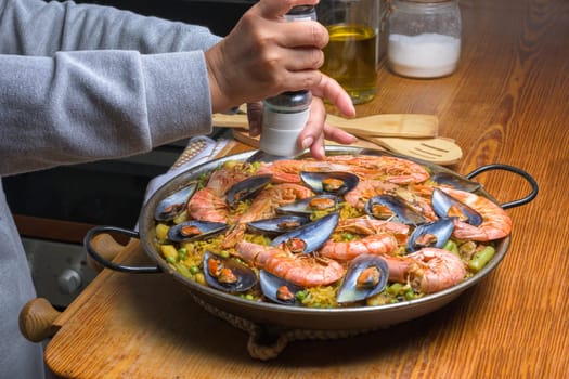 Person seasoning a paella with prawns and mussels, evoking home cooking, typical Spanish cuisine, Majorca, Balearic Islands, Spain,
