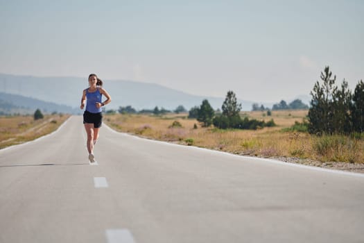 An athletic woman finds freedom and joy in a healthy lifestyle, running through a beautiful road trail at sunrise.