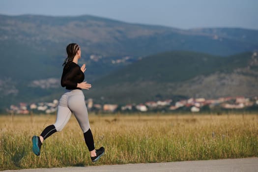 An athletic woman finds freedom and joy in a healthy lifestyle, running through a beautiful road trail at sunrise.