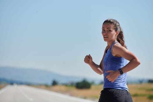 An athletic woman finds freedom and joy in a healthy lifestyle, running through a beautiful road trail at sunrise.