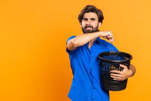 Attractive middle eastern man taking off throwing out glasses into bin after medical vision laser treatment therapy surgery looking smiling at camera. Healthy cured guy isolated on orange background