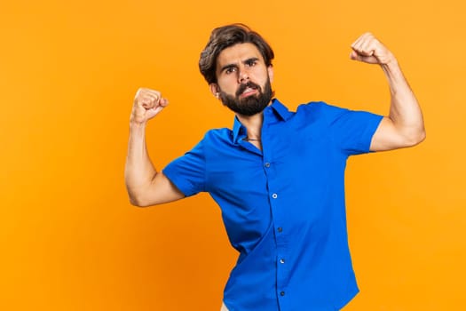 I am strong and independent. Young man showing biceps and looking confident, feeling power strength to fight for rights, energy to gain success win. Arabian guy isolated on orange studio background