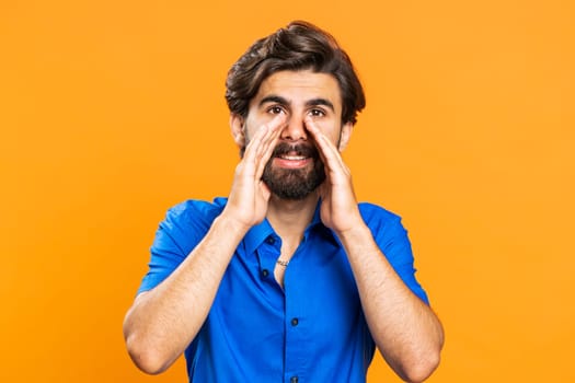 Keep my secrets, silence. Man whisper news rumors holding hands near mouth share gossip, quiet. Middle eastern guy in shirt telling interesting confidential story isolated on orange studio background
