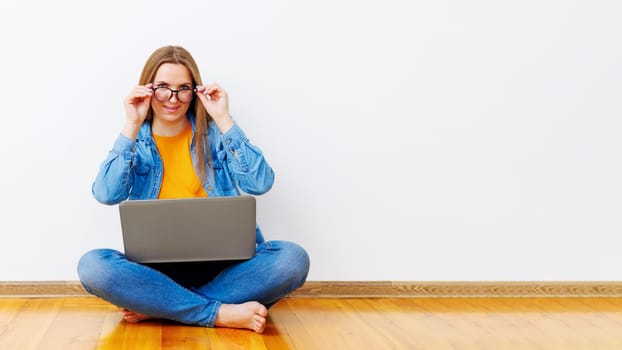 Woman sitting cross-legged on wooden floor holding laptop. Casual indoor portrait with copy space for design and banner