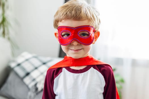 Happy young boy dressed as a superhero with cape and mask, smiling confidently.