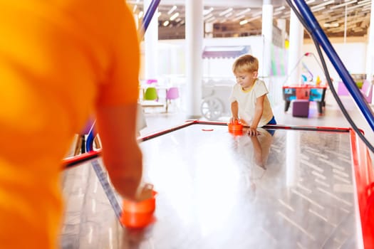 Boy playing air hockey in indoor play area. Child enjoying game in colorful recreational space. Leisure and playtime concept for design and print. Candid shot with place for text