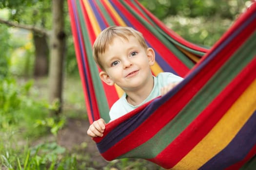 Smiling child peeking from colorful hammock. Outdoor relaxation and joy concept. Summer leisure scene. Design for greeting card, postcard