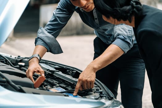 Man help woman fix the car problem. He pop up the car hood to repair the damaged part. uds