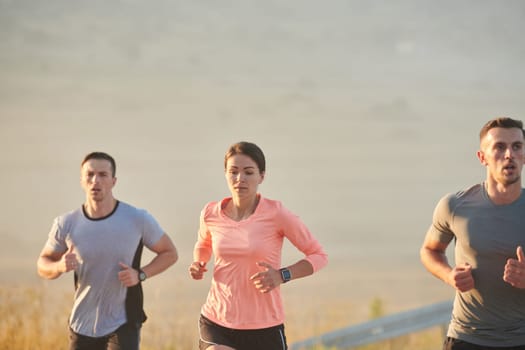 A group of friends, athletes, and joggers embrace the early morning hours as they run through the misty dawn, energized by the rising sun and surrounded by the tranquil beauty of nature.