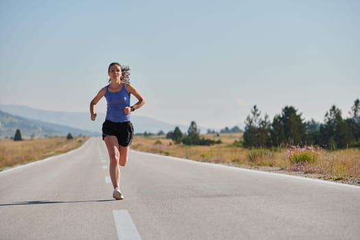 An athletic woman finds freedom and joy in a healthy lifestyle, running through a beautiful road trail at sunrise.