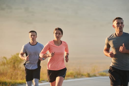 A group of friends, athletes, and joggers embrace the early morning hours as they run through the misty dawn, energized by the rising sun and surrounded by the tranquil beauty of nature.