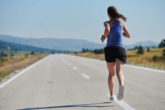 An athletic woman finds freedom and joy in a healthy lifestyle, running through a beautiful road trail at sunrise.