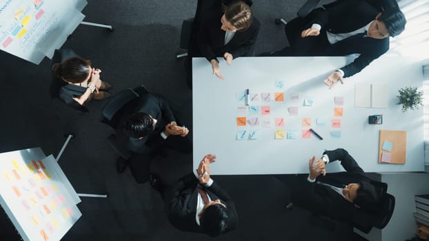 Top down aerial view of business group sharing and brainstorming idea by using sticky notes at meeting room. Investor writing marketing strategy on board while receive note from manager. Directorate.