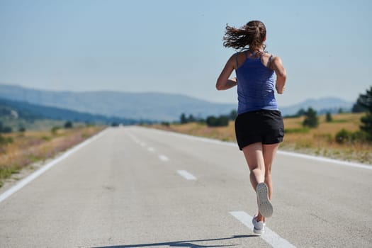 An athletic woman finds freedom and joy in a healthy lifestyle, running through a beautiful road trail at sunrise.