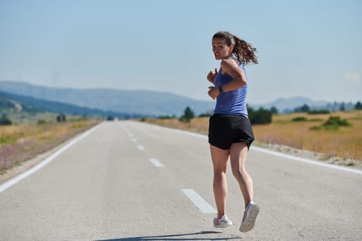 An athletic woman finds freedom and joy in a healthy lifestyle, running through a beautiful road trail at sunrise.