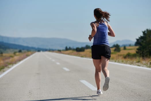 An athletic woman finds freedom and joy in a healthy lifestyle, running through a beautiful road trail at sunrise.