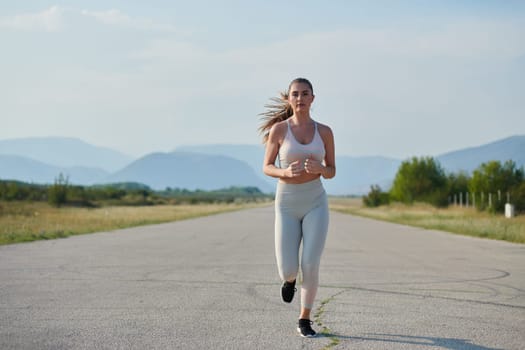 An athletic woman finds freedom and joy in a healthy lifestyle, running through a beautiful road trail at sunrise.