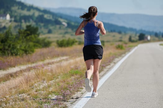 An athletic woman finds freedom and joy in a healthy lifestyle, running through a beautiful road trail at sunrise.