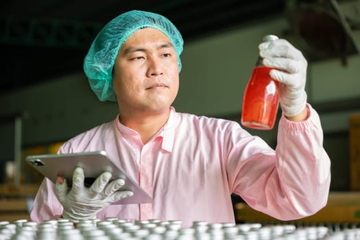 Quality control worker inspects bottles on conveyor belt in beverage factory ensuring top industry standards. Engineer and inspector collaborate on tablet for efficient production.