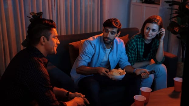 Top view of caucasian father and relaxed mother watching movie while eating snack with friend. Happy family with colleague looking at television while dad hold snack bowl at living room. Convocation.