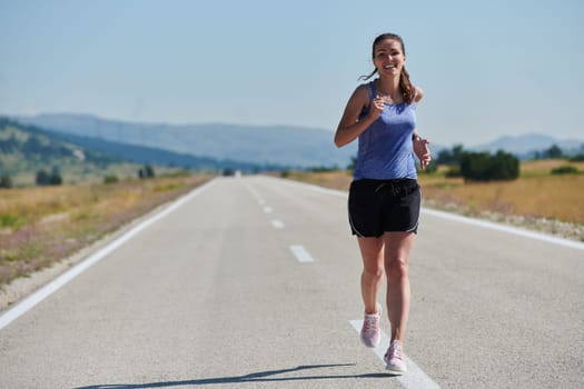 An athletic woman finds freedom and joy in a healthy lifestyle, running through a beautiful road trail at sunrise.