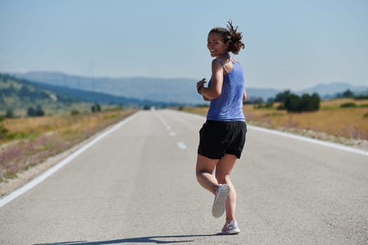 An athletic woman finds freedom and joy in a healthy lifestyle, running through a beautiful road trail at sunrise.