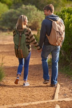 Path, hiking and happy couple holding hands in nature for holiday, travel or adventure outdoor with backpack. Rear view, man or woman trekking in the countryside on vacation, journey or date together.