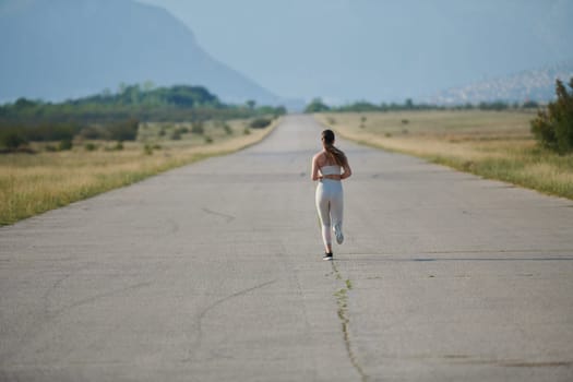 An athletic woman finds freedom and joy in a healthy lifestyle, running through a beautiful road trail at sunrise.