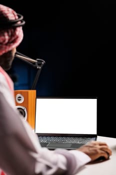 Image depicts Muslim guy working from home, sat at his desk, with an isolated chromakey template shown on his minicomputer. Young Arab man using laptop with a copyspace white screen.