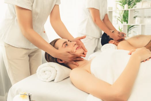 Caucasian couple enjoying relaxing anti-stress head massage and pampering facial beauty skin recreation leisure in dayspa modern light ambient at luxury resort or hotel spa salon. Quiescent