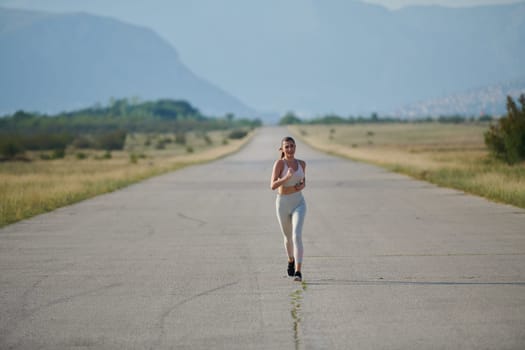 An athletic woman finds freedom and joy in a healthy lifestyle, running through a beautiful road trail at sunrise.