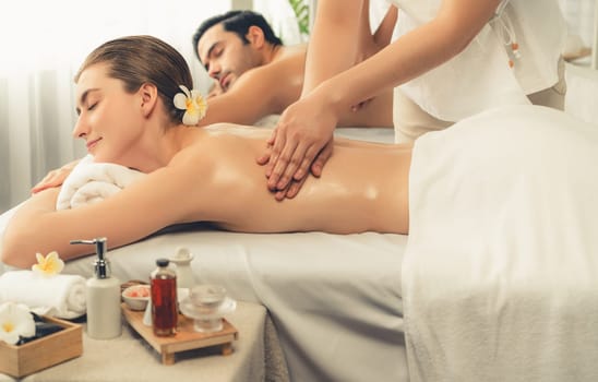 Caucasian couple customer enjoying relaxing anti-stress spa massage and pampering with beauty skin recreation leisure in day light ambient salon spa at luxury resort or hotel. Quiescent