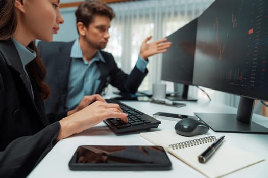 Two business traders analyzing dynamic stock market in currency rate investment program website online on two computer screens, woman checking to compare real time graph at modern office. Postulate.