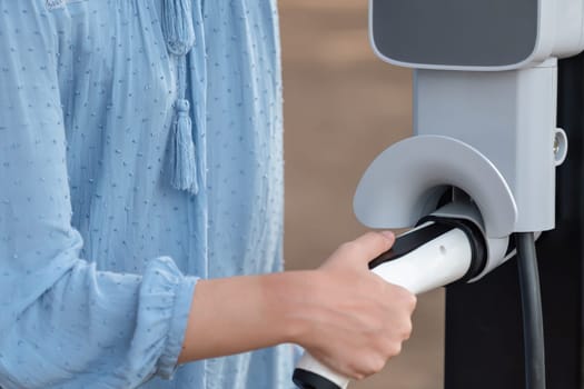 Hand insert EV charger plug into electric vehicle to recharge EV car battery from outdoor charging station. Fresh daylight environment with alternative clean and sustainable energy concept. Perpetual