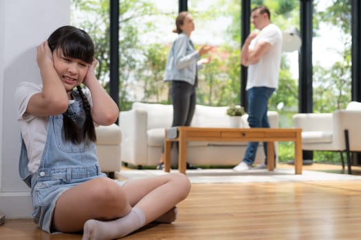 Stressed and unhappy girl huddle in corner, cover her ears with painful expression while her parent arguing in background. Domestic violence and traumatic childhood develop to depression. Synchronos