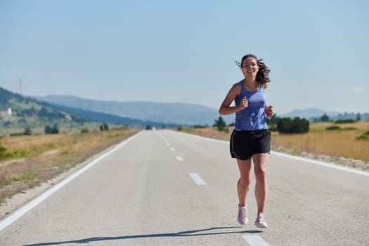 An athletic woman finds freedom and joy in a healthy lifestyle, running through a beautiful road trail at sunrise.