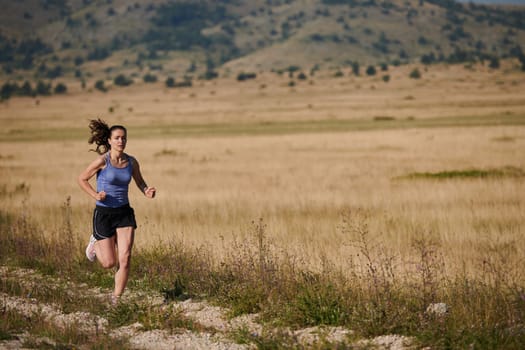 An athletic woman finds freedom and joy in a healthy lifestyle, running through a beautiful road trail at sunrise.