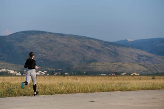 An athletic woman finds freedom and joy in a healthy lifestyle, running through a beautiful road trail at sunrise.