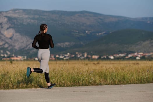 An athletic woman finds freedom and joy in a healthy lifestyle, running through a beautiful road trail at sunrise.