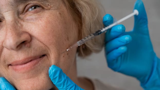 Doctor makes beauty injections in the face of an old caucasian woman