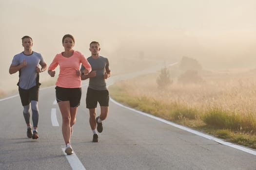 A group of friends, athletes, and joggers embrace the early morning hours as they run through the misty dawn, energized by the rising sun and surrounded by the tranquil beauty of nature.