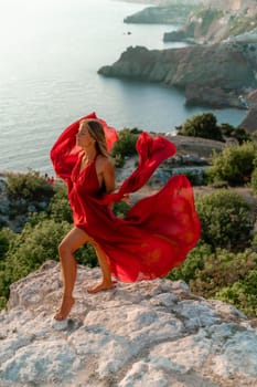 Woman sunset sea red dress, side view a happy beautiful sensual woman in a red long dress posing on a rock high above the sea on sunset